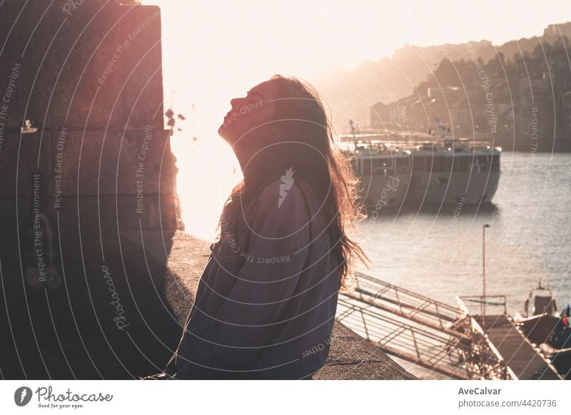 Frau, die ihre Augen schließt und nach oben schaut, während sie ausatmet und sich in den Docks der Stadt entspannt, während eines farbenfrohen Sonnenuntergangs, Konzept der psychischen Gesundheit, Tourismus