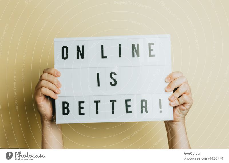 Zwei Hände halten ein Schild mit der Aufschrift "Online ist besser" vor einem pastellgelben Hintergrund, Styling- und Designkonzept, Copy Space, Online-Kauf und E-Commerce