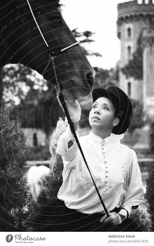 Afroamerikanische Frau streichelt Pferd auf dem Lande Jockey Haustier elegant Pflanze Hut ernst Körperhaltung schwarz Afroamerikaner Erwachsener selbstbewusst