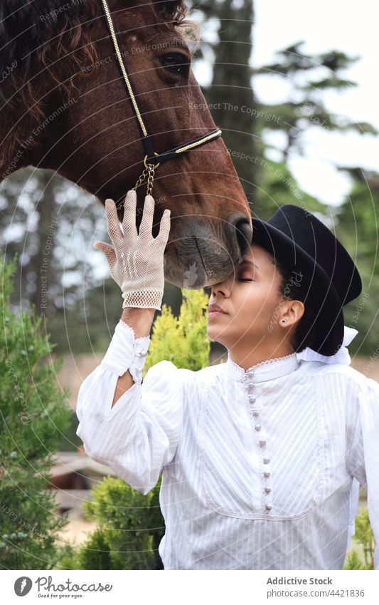 Afroamerikanische Frau streichelt Pferd auf dem Lande Jockey Haustier elegant Pflanze Hut ernst Körperhaltung schwarz Afroamerikaner Erwachsener selbstbewusst