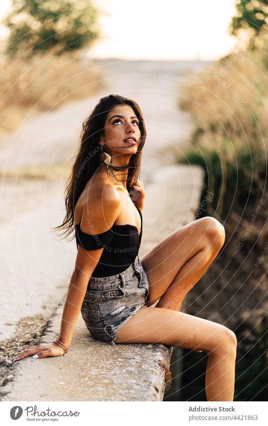 Frau im Sommeroutfit auf Brücke sitzend Stil Landschaft sorgenfrei Barfuß Mode Aussehen Outfit attraktiv jung hispanisch ethnisch brünett Shorts Top positiv