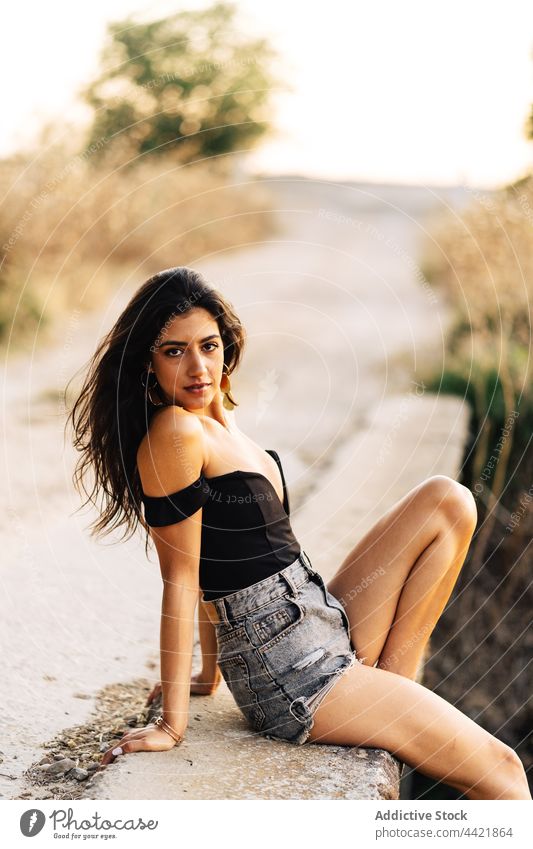 Frau im Sommeroutfit auf Brücke sitzend Stil Landschaft sorgenfrei Barfuß Mode Aussehen Outfit attraktiv jung hispanisch ethnisch brünett Shorts Top positiv