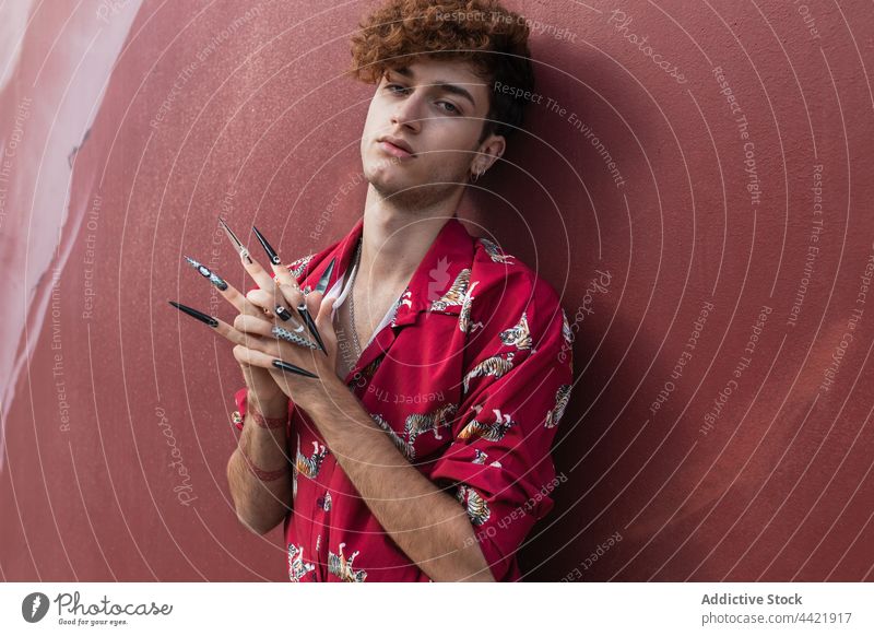 Cooles schwules Modell mit falschen Nägeln an der Wand Homosexualität Maniküre Stil Hände gefaltet Individualität ignorant Mann Porträt nageln kreativ Design