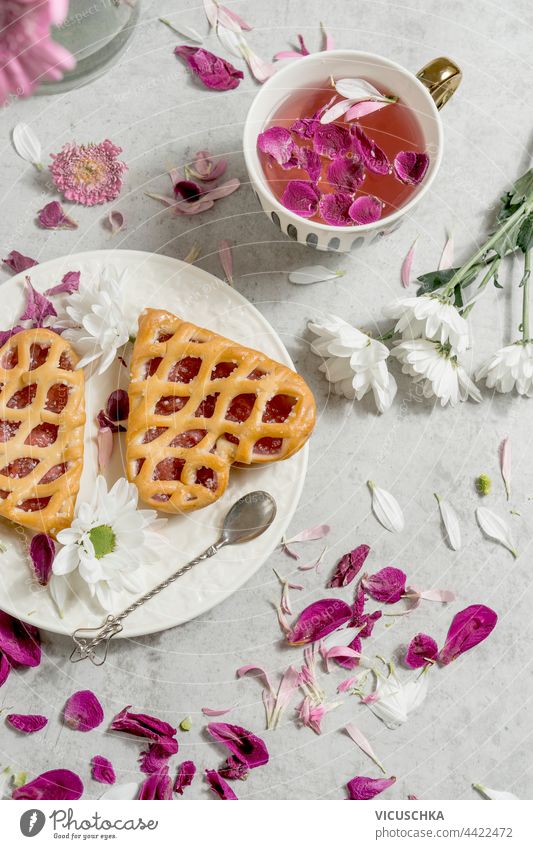 Herzförmige Torten mit Marmelade und Blumentee auf einem hellen Tisch mit Blütenblättern. Ansicht von oben geformt Kuchen Tee Licht Draufsicht Frühstück lecker