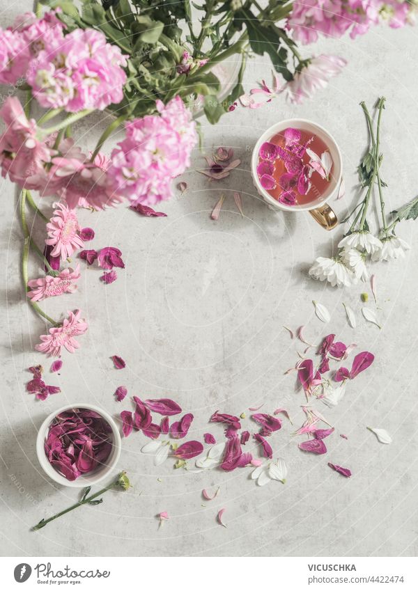 Tasse mit rosa Blumen Tee auf hellem Schreibtisch mit Pfingstrosen Blumenstrauß und Blütenblätter . Ansicht von oben. Rahmen Licht Haufen Draufsicht schön