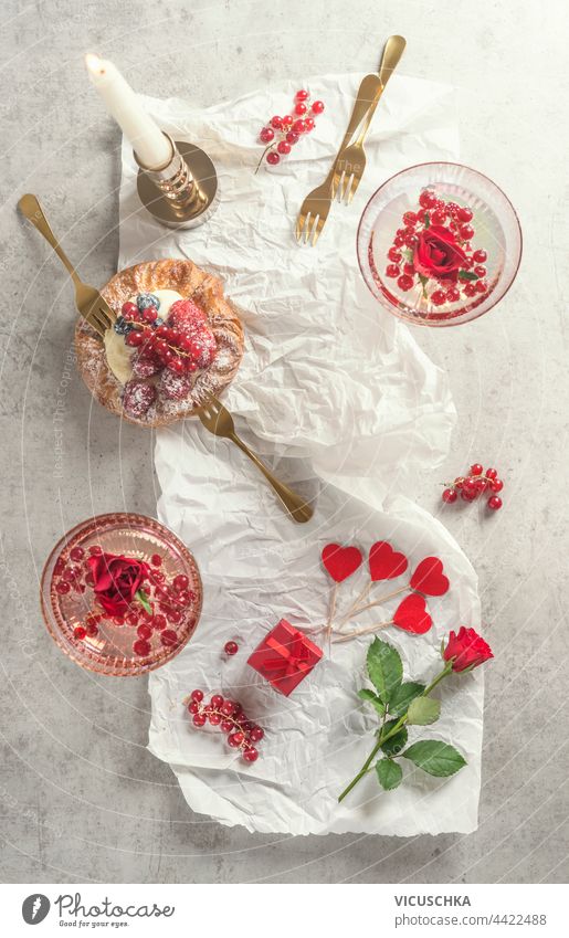 Cocktailgläser mit Champagner, Torte und vielen roten Herzen mit Rosenblüten. Ansicht von oben. Romantisches Frühstück Brille Kuchen Roséwein Draufsicht