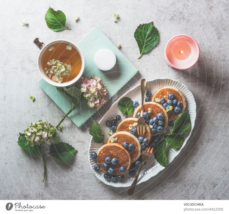 Ästhetisches Frühstück mit Blaubeerpfannkuchen, Tasse Tee und Kerze mit Hortensienblüten. Ansicht von oben Ästhetik Blaubeeren Pfannkuchen Blumen Draufsicht