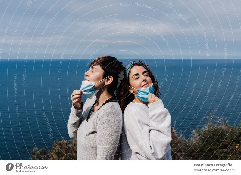 Zwei kaukasische Frauen nehmen im Freien die Gesichtsmaske ab, atmen und halten sozialen Abstand in der Pandemie während des Corona-Virus. Natur und Berg Atem