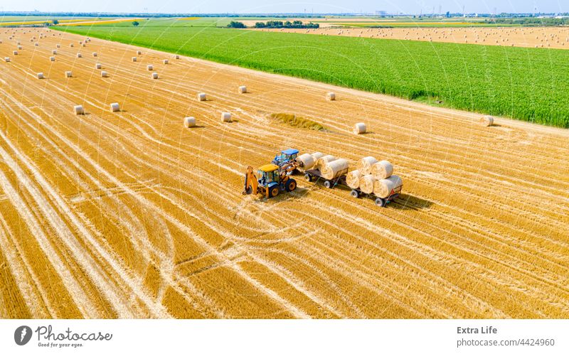 Blick von oben auf ein landwirtschaftliches Feld, das Rundballen aus Stroh sammelt Antenne Ackerbau Ballen Ladung führen Müsli bedeckt umhüllt Bagger Landwirt