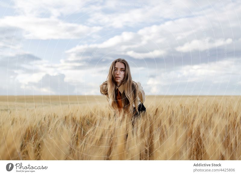 Millennial-Frau zwischen Weizenähren im Feld Natur Ackerbau vegetieren Ackerland emotionslos Starrer Blick Porträt Landschaft Wiese wachsen Müsli Korn wolkig
