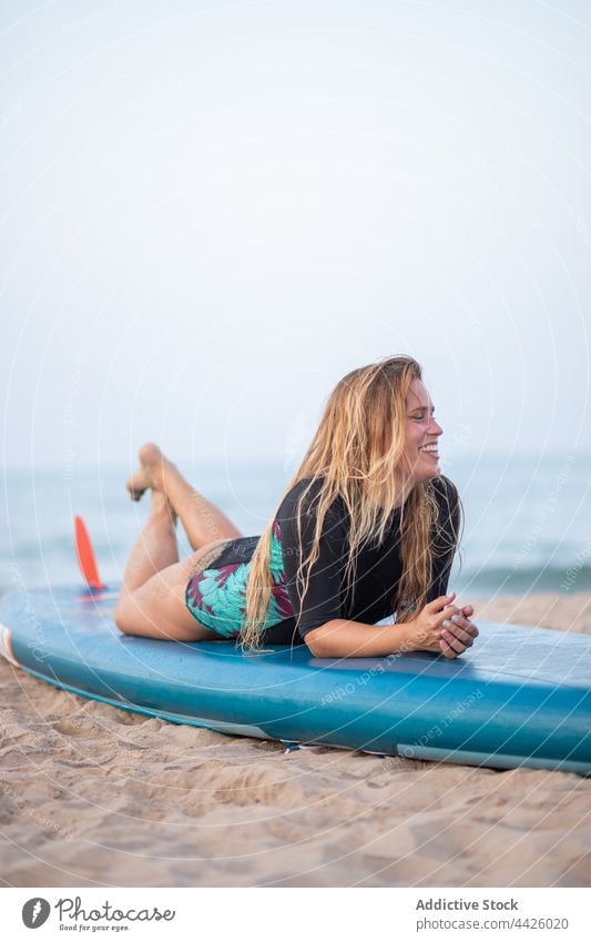 Fröhliche Frau auf SUP-Brett am Strand liegend Surfer Paddelbrett Lügen Zusatzplatine Badeanzug Lächeln Meeresufer MEER Sommer Ufer Urlaub Badebekleidung