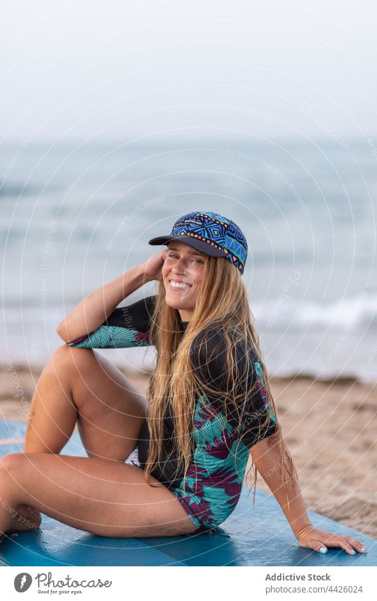 Fröhliche Frau sitzt auf einem SUP-Board am Strand Surfer Paddelbrett Zusatzplatine Badeanzug Lächeln Meeresufer MEER Sommer Ufer Urlaub Badebekleidung Hut