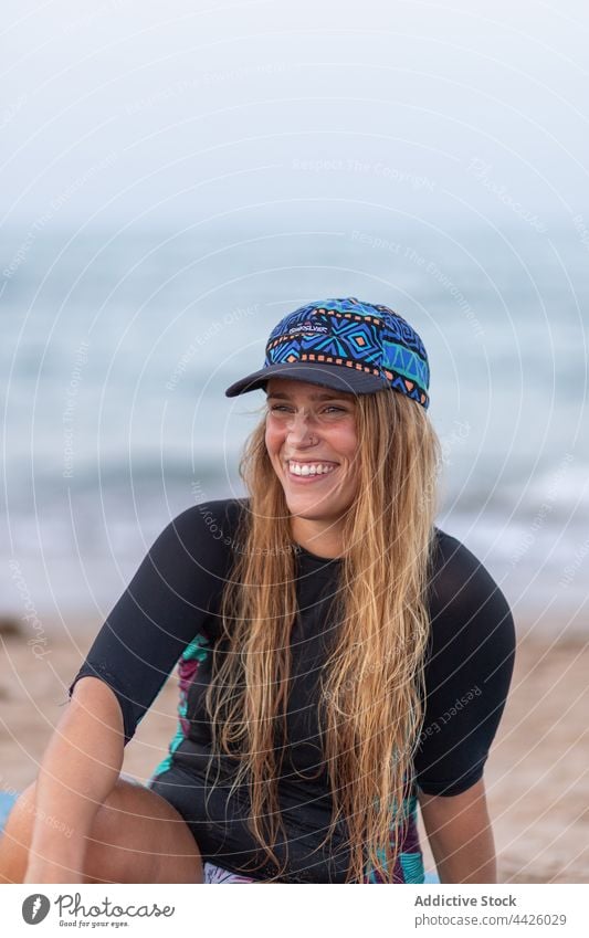 Fröhliche Frau sitzt auf einem SUP-Board am Strand Surfer Paddelbrett Zusatzplatine Badeanzug Lächeln Meeresufer MEER Sommer Ufer Urlaub Badebekleidung Hut