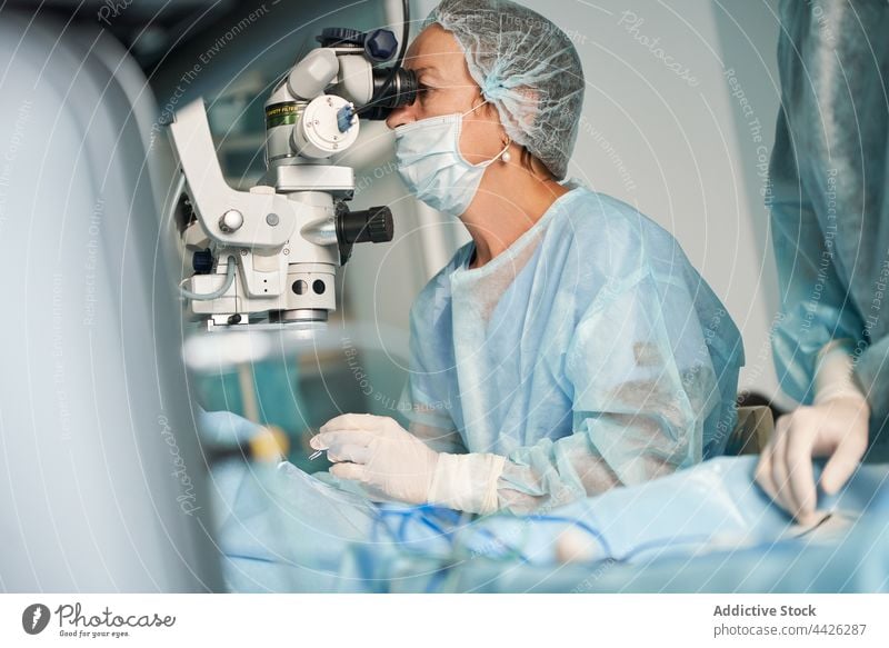 Chirurg schaut durch Mikroskop gegen Erntehelfer in Klinik durchsehen untersuchen optisch Instrument achtsam Frau Uniform Ornament geblümt Verschlussdeckel