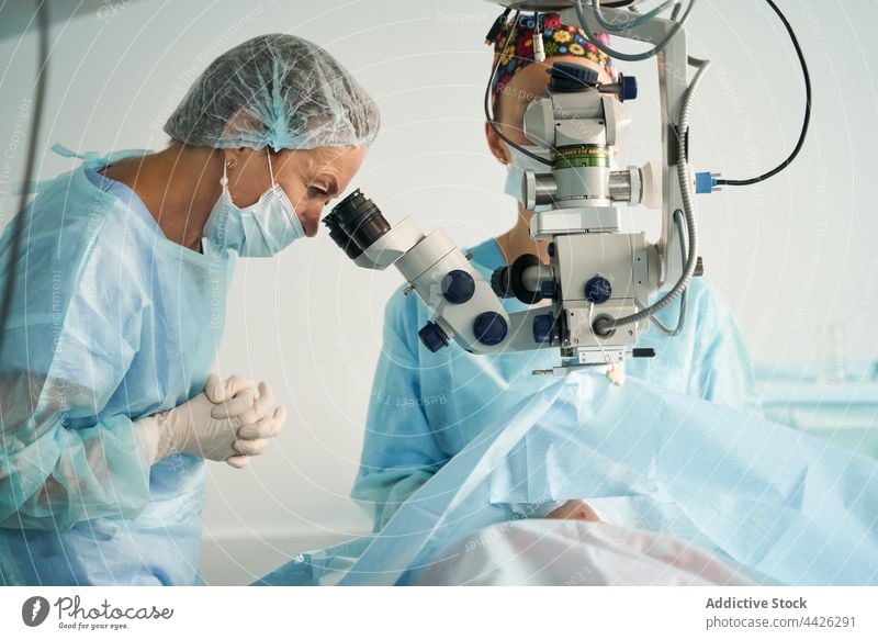 Chirurg schaut durch Mikroskop gegen Erntehelfer in Klinik durchsehen untersuchen optisch Instrument achtsam Frau Uniform Ornament geblümt Verschlussdeckel