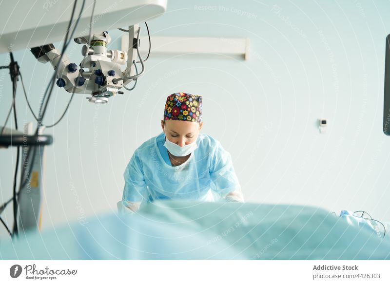 Chirurgische Krankenschwester in steriler Uniform bei der Vorbereitung des Operationssaals Arbeit Krankenpfleger achtsam Mikroskop behüten nach vorne lehnen