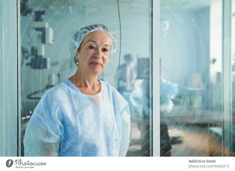Lächelnder Chirurg in medizinischer Uniform vor einer Glaswand in einer Klinik Arzt chirurgisch freundlich Beruf Frau Porträt Krankenhaus herzlich professionell
