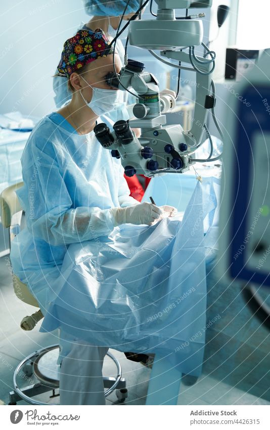 Augenarzt schaut durch das Mikroskop während einer Augenoperation in der Klinik Ophthalmologe Operation durchsehen Okular achtsam Instrument geduldig Frau