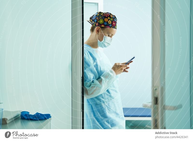 Chirurg in Uniform chattet im Krankenhaus mit seinem Smartphone plaudernd Internet online Pause Frau benutzend Gerät Mundschutz steril professionell Klinik