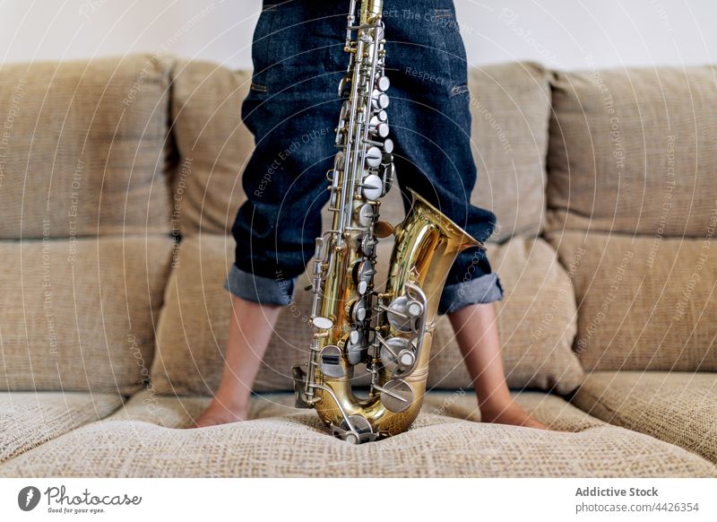 Unbekanntes Mädchen mit Saxophon auf der Couch im Haus Kindheit Musik Kunst klassisch nachdenken Fenster Liege heimwärts Sofa Barfuß Hut gesamt Jeansstoff