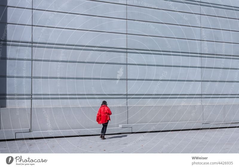 Die rote Jacke der jungen Frau leuchtet vor der strukturierten Fassade des modernen Museums Architektur urban Wand Linien Geometrie allein leuchtend Frühling