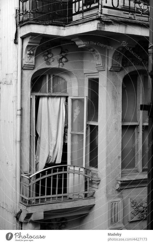 Offenes Fenster mit improvisiertem Vorhang und kleinem Balkon eines alten Haus in den Gassen von Taksim in Istanbul am Bosporus in der Türkei, fotografiert in klassischem Schwarzweiß