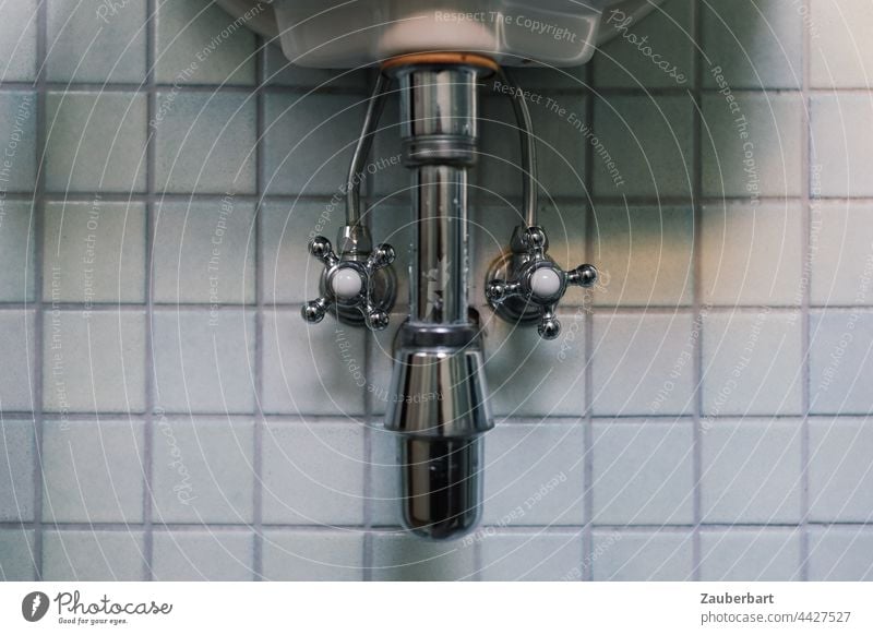 Siphon, Wasserhähne, Wasserleitungen eines Waschbeckens vor kleinen quadratischen Fliesen Wasserhahn Bad Badezimmer waschen Waser Leitung Abwasser Porzellan