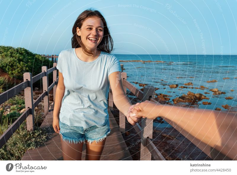 Glückliche Teenager-Mädchen laufen auf dem Bürgersteig am Meer bei Sonnenuntergang Junge Frau Hand Attrappe Lächeln T-Shirt Jugendlicher blau Kaukasier MEER
