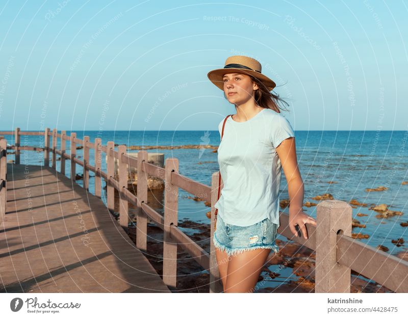 Teenager-Mädchen steht auf einer Holzbrücke am Meer Sonnenuntergang MEER Strohhut Attrappe Kaukasier Jugendlicher blau Bürgersteig im Freien Urlaub reisen