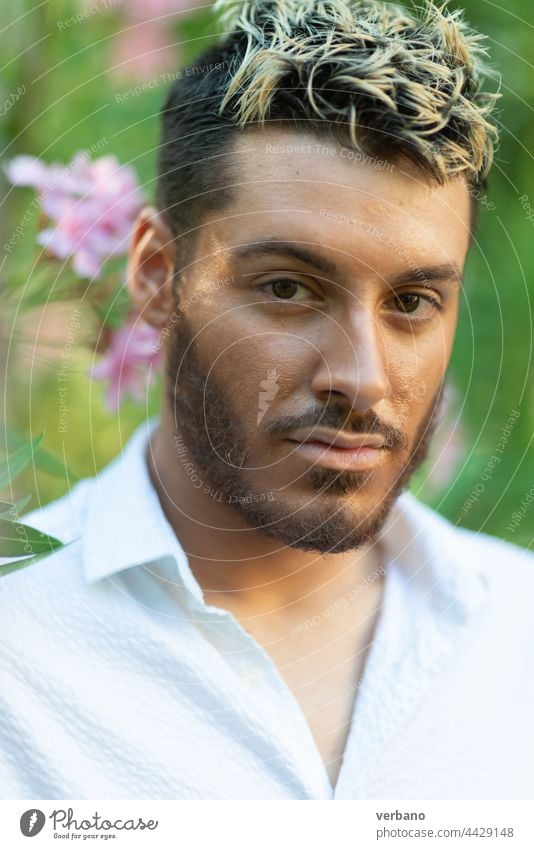 Kaukasischer junger Mann mit weißem Hemd in einem Park im Sommer mit rosa Blumen und grünen Blättern unscharf Tänzer schwul Glück Lifestyle Person Stolz
