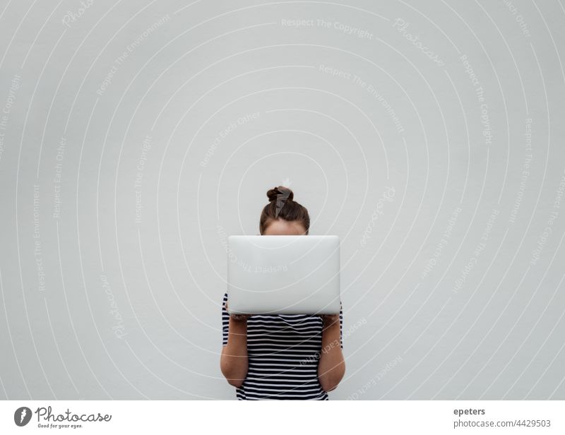 Junge Frau in Jeans und T-Shirt hält sich einen silbernen Laptop vor das Gesicht braune Haare Computer selbstbewusst Textfreiraum