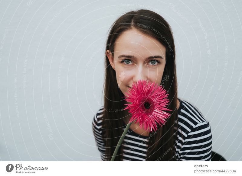 Lächelnde junge Frau versteckt sich hinter einer Blume, die ihr Gesicht teilweise verdeckt hell braune Haare lässig Textfreiraum freundlich Gerbera grüne Augen