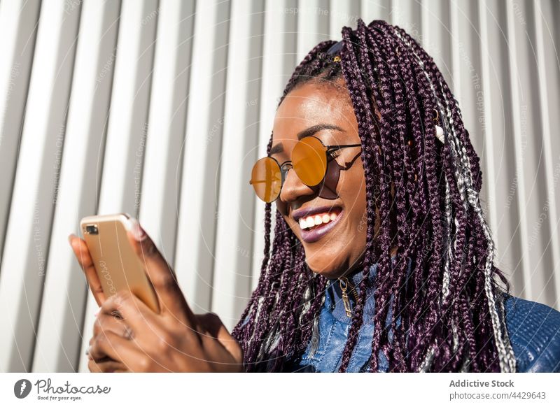 Schwarze Frau mit Zöpfen benutzt Smartphone benutzend Afro-Look Stil heiter urban trendy Apparatur Geflecht Afroamerikaner schwarz ethnisch Mobile jung Hipster