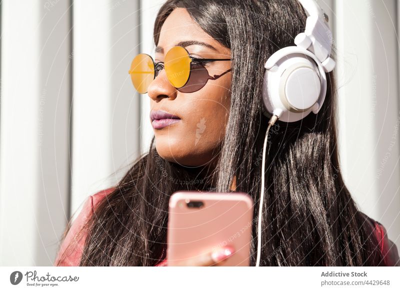 Stilvolle schwarze Frau mit Smartphone hört Musik Kopfhörer urban zuhören trendy Apparatur Mode Afroamerikaner ethnisch jung Telefon Mobile Sonnenbrille modern