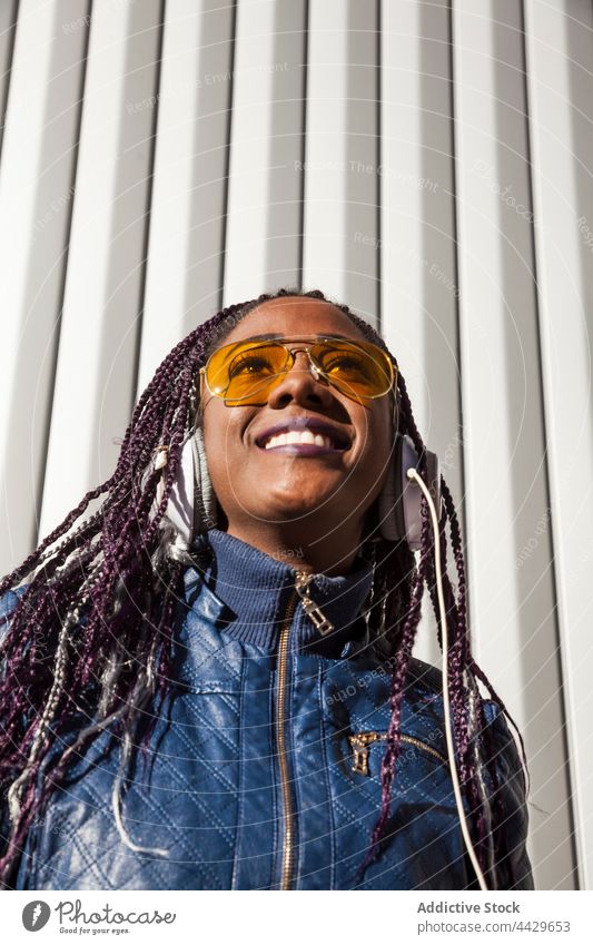 Fröhliche schwarze Frau beim Musikhören Kopfhörer zuhören Stil trendy heiter Kälte Glück genießen Afroamerikaner ethnisch Afro-Look Geflecht Sonnenbrille jung