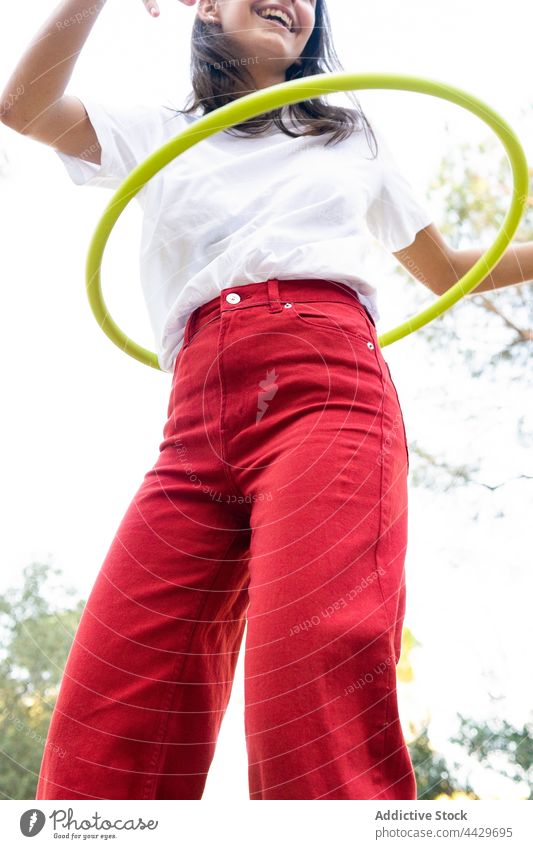Lächelnder, aktiver Teenager, der im Park einen Reifen schwingt verdrehen Hula Erholung Freizeit froh genießen freie Zeit Aktivität rot Jeanshose Inhalt