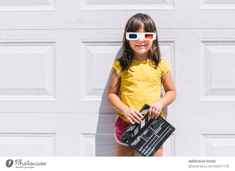 Trendiges Kind mit 3D-Brille, das eine Klappe hält und an der Wand steht dreidimensional Lächeln unterhalten 3d Spaß Glück Freude lässig Mädchen Filmklappe
