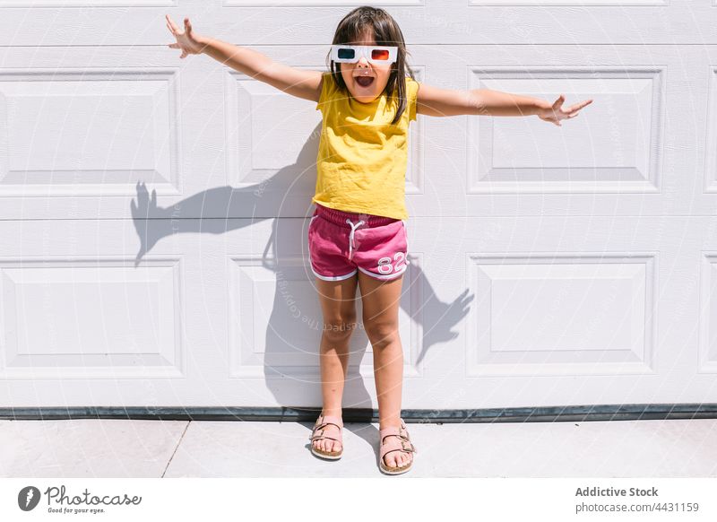 Glückliches trendiges Kind mit 3D-Brille an der Wand stehend Mädchen dreidimensional unterhalten 3d Spaß Lächeln Showtime Freude Waffen ausgestreckt lässig