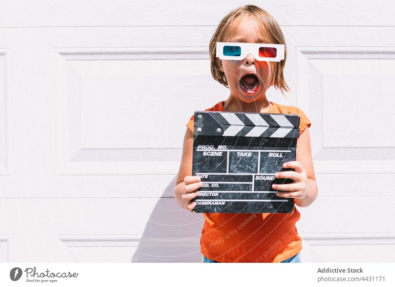 Trendiges Kind mit 3D-Brille, das eine Klappe hält und an der Wand steht dreidimensional erstaunt unterhalten 3d Spaß Freude Erstaunen lässig Mädchen Filmklappe