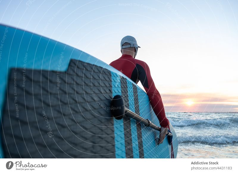 Mann mit Paddelbrett im Wasser zum Surfen Zusatzplatine Surfer Meeresufer Neoprenanzug Strand männlich Surfbrett Sport Hut Brandung MEER Seeküste Ufer