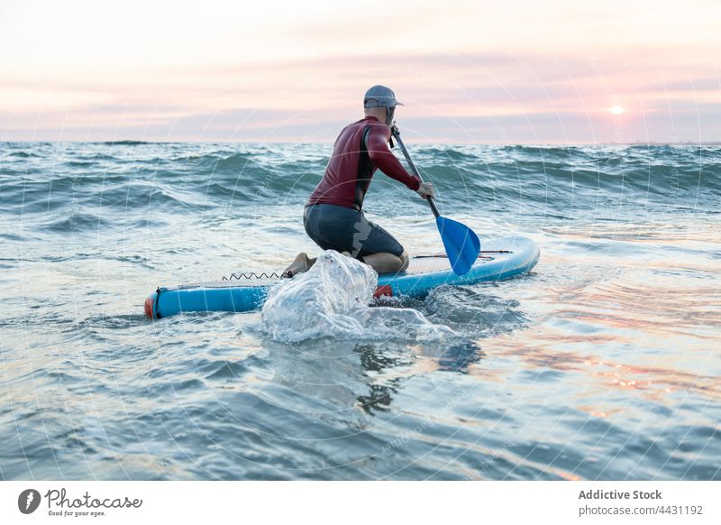 Mann mit Paddelbrett im Wasser zum Surfen Zusatzplatine Surfer Meeresufer Neoprenanzug Strand männlich Surfbrett Sport Hut Brandung MEER Seeküste Ufer