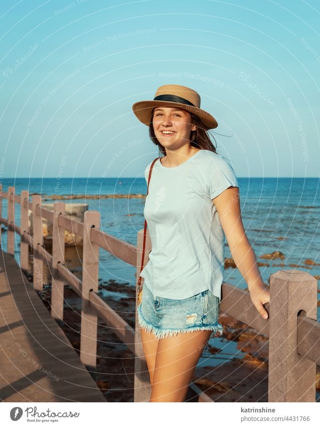 Teenager-Mädchen steht auf einer Holzbrücke am Meer Sonnenuntergang MEER Strohhut Attrappe Kaukasier Jugendlicher blau Bürgersteig im Freien Urlaub reisen