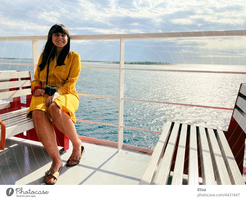 Eine Frau in einem gelben Kleid sitzt bei Sonnenschein auf einer Bank auf einer Fähre Schiff Meer Ferien & Urlaub & Reisen Sommer lächeln Reling Passagierschiff