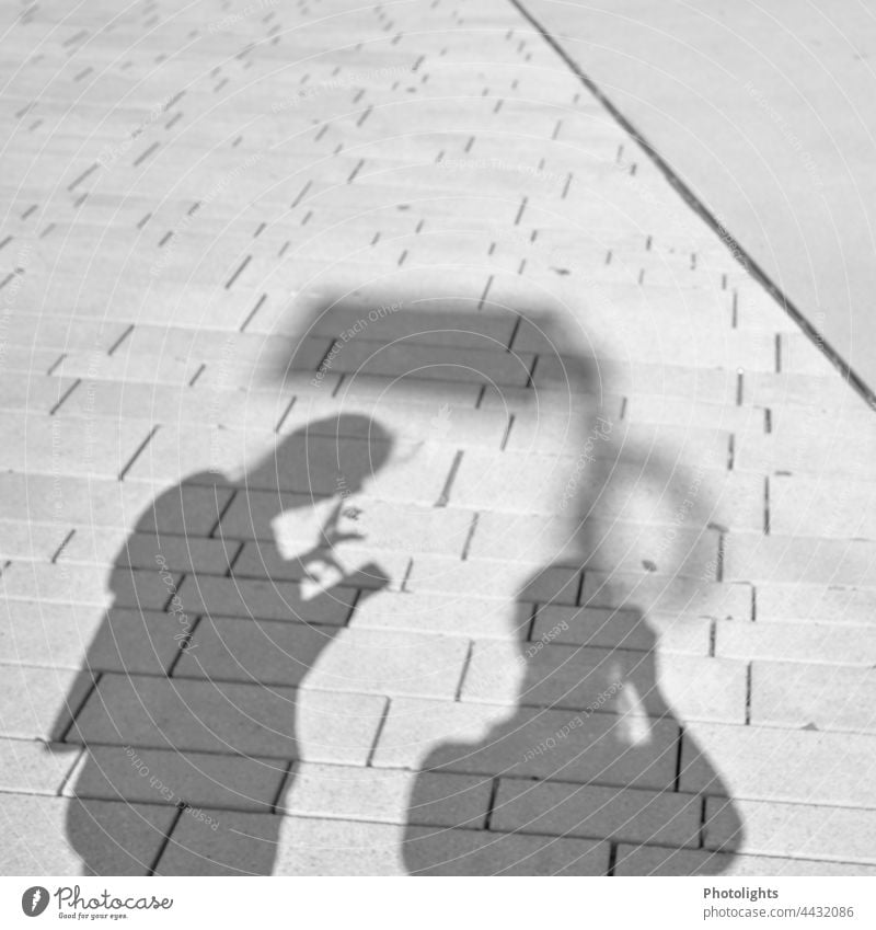 Schattenspielerei 2 Personen Kontrast Mensch Smartphone Zusammen Straße Stadt Pflaster Boden Außenaufnahme Menschen Silhouette gemeinsam Spaziergang gehen
