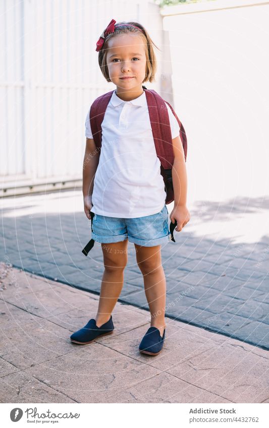 Schulmädchen in Freizeitkleidung mit Rucksack auf städtischem Gehweg neugierig Kindheit zurück zur Schule Straßenbelag Steinwand urban charmant verträumt