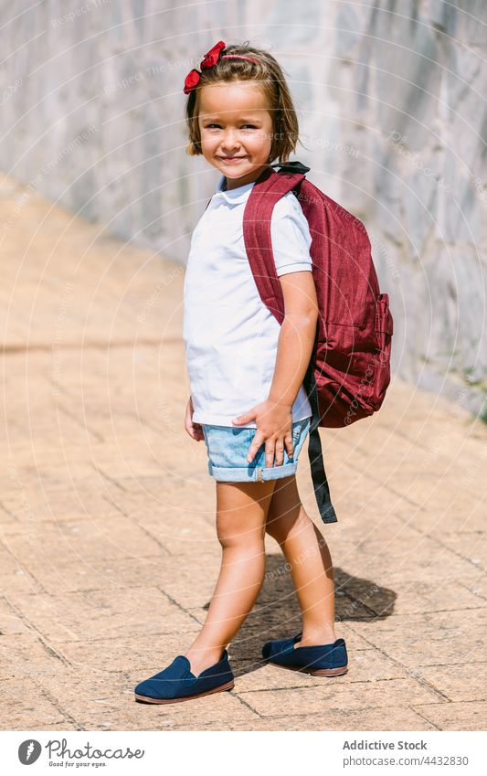 Schulmädchen in Freizeitkleidung mit Rucksack auf städtischem Gehweg neugierig Kindheit zurück zur Schule Straßenbelag Steinwand urban charmant verträumt