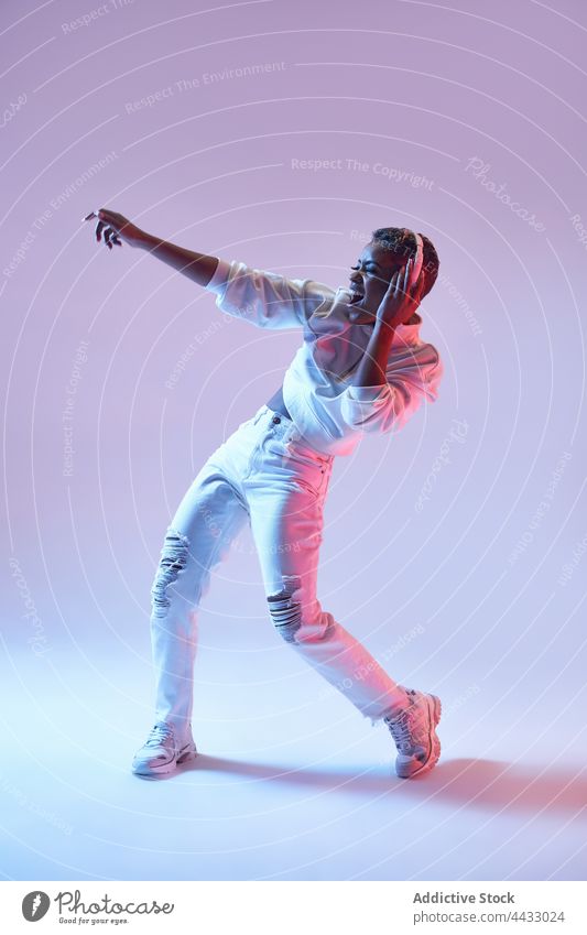 Aktive schwarze Tänzerin mit Headset tanzt Hip-Hop auf hellem Hintergrund Choreographie Energie Bewegung Mode Frau benutzend Apparatur Tanzen aktiv Gerät