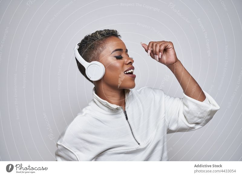 Aktive schwarze Tänzerin mit Headset tanzt Hip-Hop auf grauem Hintergrund Choreographie Energie Bewegung Mode Frau benutzend Apparatur Tanzen aktiv Gerät