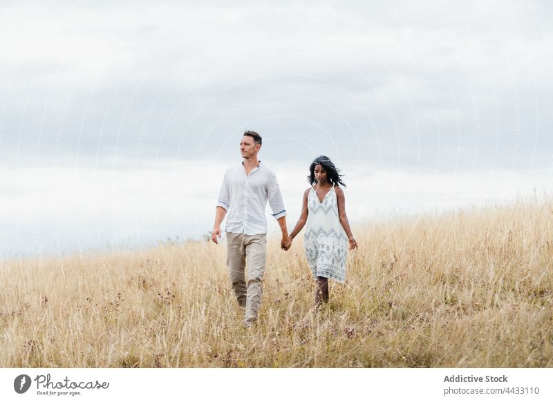 Ein gemischtrassiges Paar hält sich auf dem Lande an den Händen Händchenhalten Partnerschaft Liebe Seelenverwandter Spaziergang Feld Himmel wolkig Landschaft