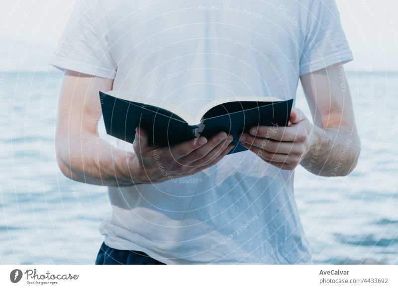 Nahaufnahme eines Mannes, der ein Buch hält, während er liest, religiöse und Studienkonzepte, Strand und heller Tag Beteiligung lesen Literatur Erholung